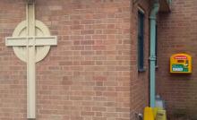 Cross on wall and defibrillator cabinet.